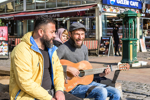 Istanbul, Turkey - December 29, 2022: Two men, one playing guitar and singing, the other listening intently on a city street corner.