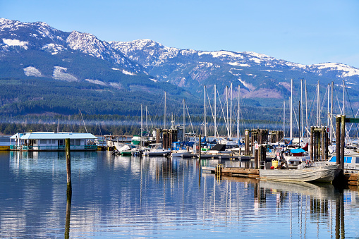 Deep Bay, Canada – March 16, 2024: The various boats moored at the Deep Bay Marina with bright reflections in the ocean water and distant mountains