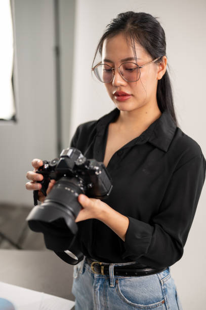 istock A confident, experienced Asian female photographer is adjusting her DSLR camera, preparing photoshoot equipment, and working in the studio. 2114050181