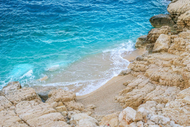 istock Small waves gently lap the shore under the bright sun. Clear blue-green waters, light gray rocks, sandy beaches, a serene and secluded oasis with only a few people enjoying the peaceful scenery. 2114066223