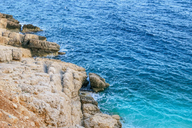 Small waves gently lap the shore under the bright sun. Clear blue-green waters, light gray rocks, sandy beaches, a serene and secluded oasis with only a few people enjoying the peaceful scenery.