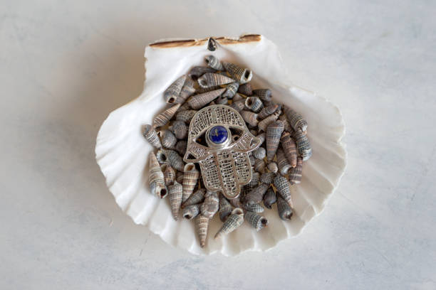 A stunning silver Hamsa hand featuring a mesmerizing blue evil eye charm, representing protection, displayed against a tranquil background of delicate white seashells.