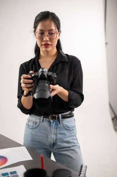 istock A confident, experienced Asian female photographer is adjusting her DSLR camera, preparing photoshoot equipment, and working in the studio. 2114095242