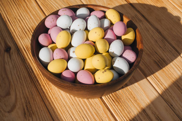 Multi-colored chocolate decorative eggs in wooden plate on a wooden table. Happy Easter background. Top view
