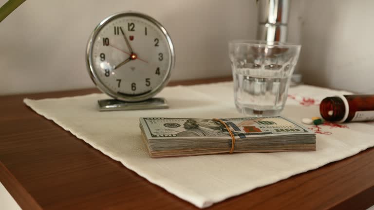 Stack of US dollar banknotes and drugs on night stand