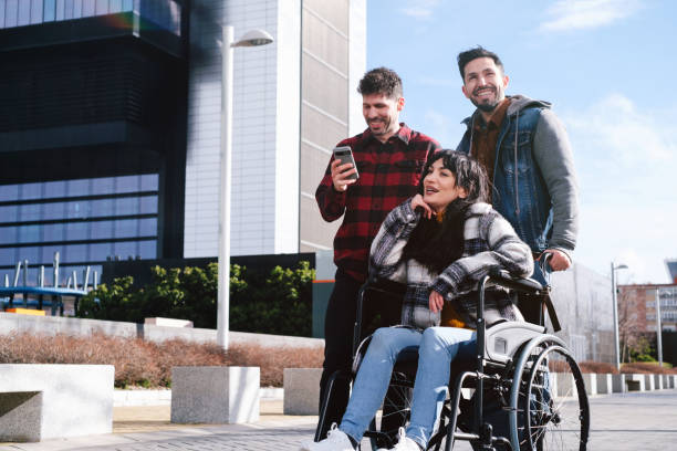 Two friends share content on a smartphone with a woman in a wheelchair, enjoying technology together outdoors.