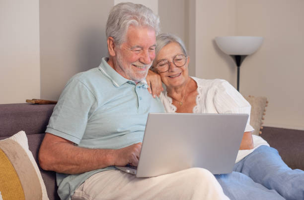 istock Cheerful senior couple relaxing on sofa, using laptop technology, enjoying happy moments together in good mood and harmony 2114123804