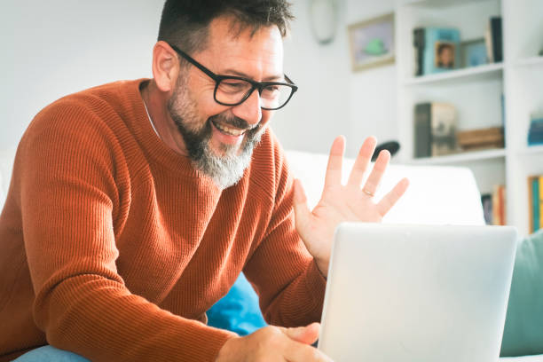 istock One man alone at home sitting on sofa doing video call with laptop and internet connection. Concept of remote work and distance call online. Mature male people and technology indoor leisure activity 2114127486