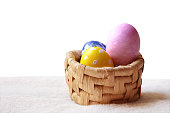 Colorful hand painted Yellow, blue and pink ornate Easter eggs in a small jute wicker basket like nest over bright off white cream colored fur carpet or furry rug background for Easter holidays celebration with copy space