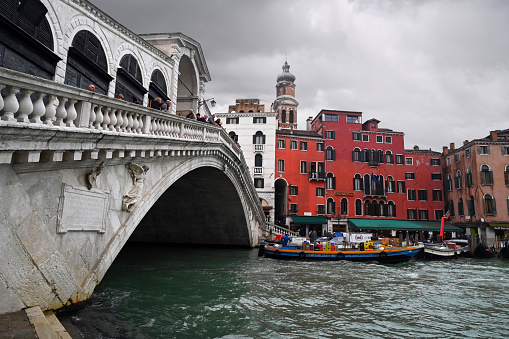 Venice, Italy, march 12, 2024 : Rialto Bridge with cloudy sky and a boat on Grand Canal