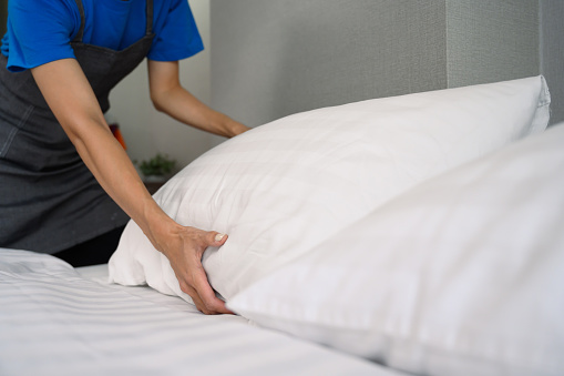 Young woman making bed at home or in hotel room. Housekeeping and cleaning service concept.