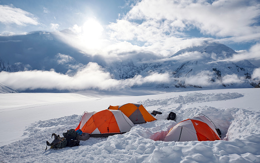 Tents in base camp on Denali during sunset, there are clouds above the glacier