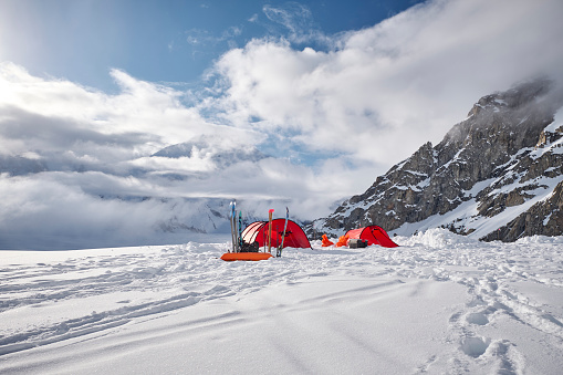 Tents in base camp on Denali during sunset, there are clouds above the glacier