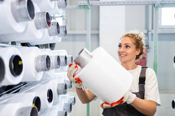 istock Female textile factory worker changing thread spool on industrial knitting machine. 2114201640