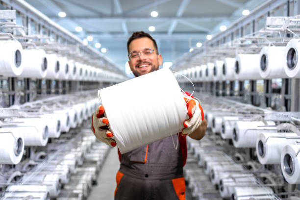 istock Experienced textile factory worker holding thread spool and and standing by industrial knitting machine. 2114212398