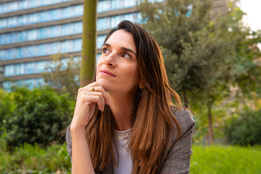 Thoughtful business woman with business woman results sitting on the street outside the office building, a mature boss staring into infinity with thoughtful face.