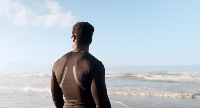 Surfer, summer and person walking on beach to check waves and current for morning surf and freedom in nature. Holiday, sea and black man getting ready for water in swimsuit in hawaii for adventure