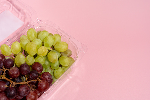 Green and red grapes in a clear container on pink background