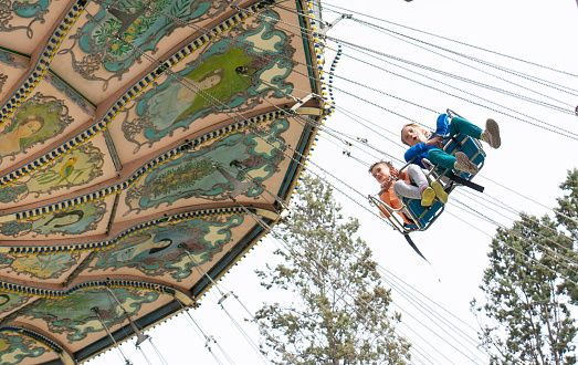 Two children riding a flying swing attraction at an amusement park with copy space