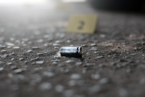 Pistol bullet shell on cement floor with blurred number two yellow paper near car wheel, concept for investigation and crime by using gun, soft focus.