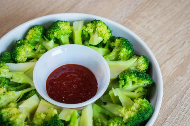 Blanched broccoli and vinegared red chili pepper paste on wood texture background.