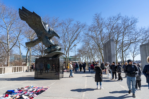 Battery Park, Manhattan, New York, USA - March, 2024. Tourists near the Bald eagle statue, by Albino Manca, part of the East Coast Memorial.