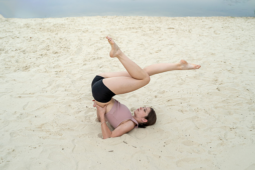 Slim woman in sportwear practice yoga on the sand beach near lake in summer. Sport healthy lifestyle