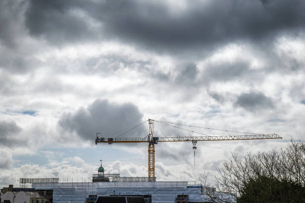 Construction crane above flame retardant scaffold sheeting wrapped apartments building during insulation in england uk.