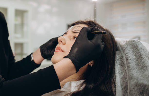 istock Changing the shape of the brows. Stylist measuring the eyebrows with the ruler. Micropigmentation work flow in a beauty salon. Woman having her eye brows tinted with Semi-permanent makeup 2114367681