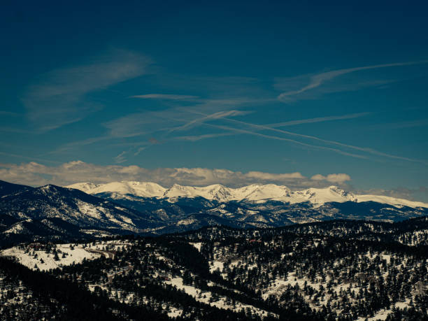 Some snow covered hills below dramatic mountain peaks and cloudy sky