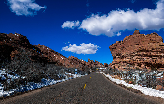 A paved road winding through red rock formations, framed by snow