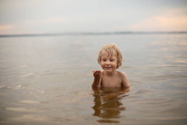 A three-year-old fair-haired boy bathes outdoors on a summer evening in the water, Holidays with children, restoration and relaxation in nature, development of children's scientific and cognitive activity in the open air, filling with joy and emotions, happy childhood and restoration of mental health