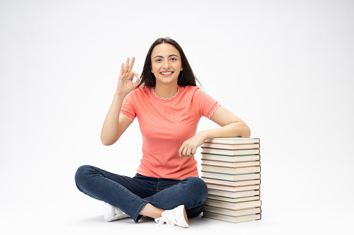 Full length body size photo of young girl book stack relaxation sitting on floor wearing jeans denim pink t-shirt footwear isolated over white background