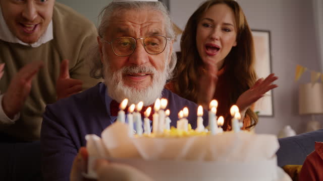Elderly male blowing on burning candles on birthday cake