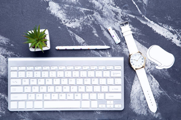 Computer keyboard with green plant, wrist watch and speech bubble on wooden table