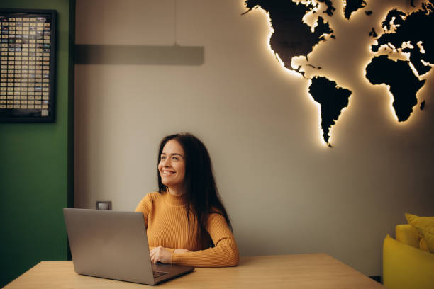 istock Female tourist agent looking at camera while working at desk with best hotels for rest on computer in travel agency. Vacation, tourism and journey. Trip booking. 2114424350