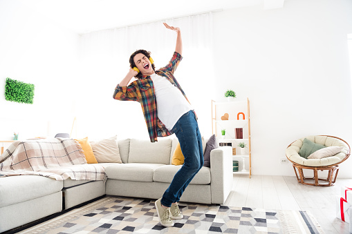 Full length photo of excited cheerful guy dressed checkered shirt dancing listening music headphones indoors house home room.
