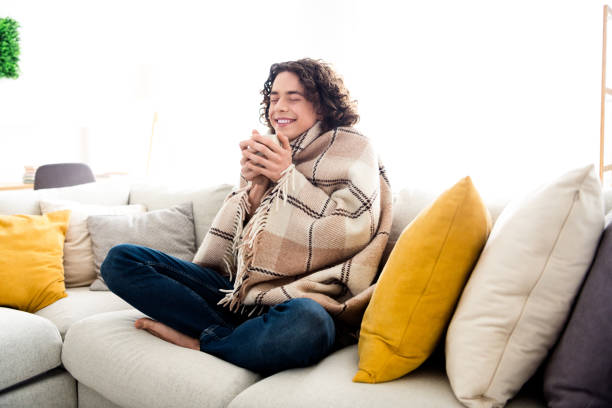 Photo of positive good mood guy rolling checkered blanket drinking hot coffee feeling cold indoors house home room.