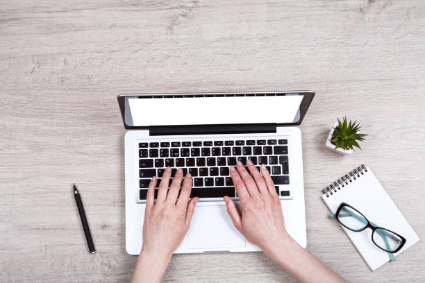 istock Woman working on laptop computer with notepad and green plant on wooden table 2114441754