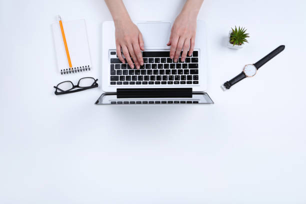 istock Woman working on laptop computer with notepad, watch and green plant on white background 2114444966