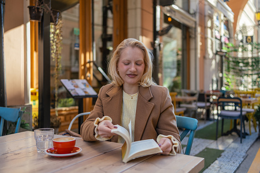 Photo of young woman sitting outdoor and reading a book