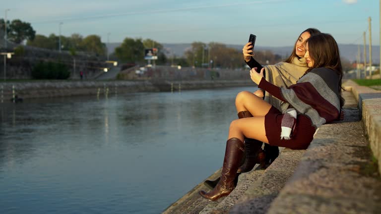 Two Young Elegant Women Taking Selfies By The River On The Quayside