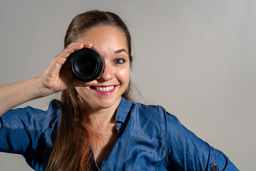Young woman with a photographic lens on her eye. Surprised young photographer looking through a lens. Young woman looking smiling through a photography lens