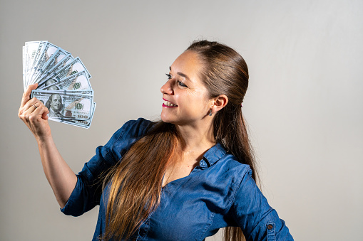 Delighted young woman holding a pile of banknotes in her hands. Young woman looking at the banknotes in her hands with happiness. Happy woman with a pile of banknotes in her hands