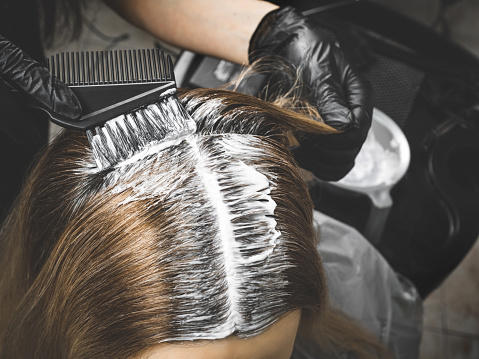 Close up of colorist dyes hair of woman with brush and foil in beauty salon