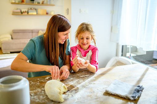 Smiling mother and daughter preparing dough in kitchen at home.