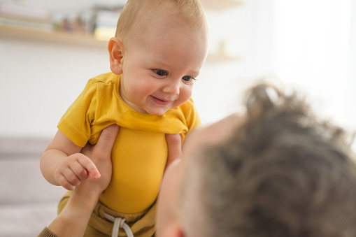 Close-up of father is lifting smiling baby son into the air.
