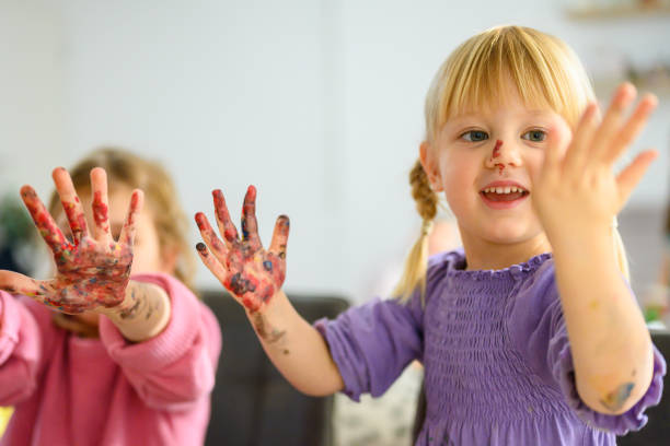 Smiling cute girls showing colorful hands while standing at home.