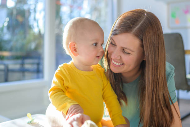 Smiling mother playing with her baby boy in living room.