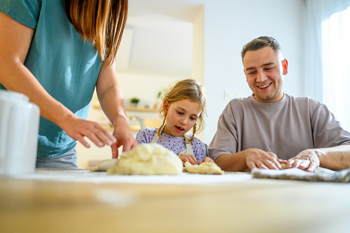 Smiling family preparing dough for bread at home.